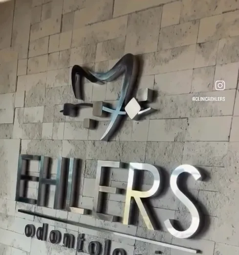 Logo EHLERS odontologia em aço sobre parede de pedra na recepção da clínica